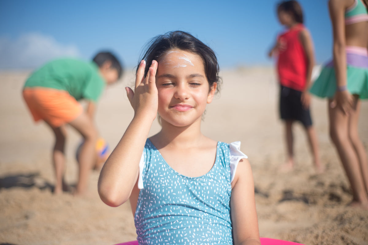 Girl applying mineral sunscreen to her forehead at the beach
