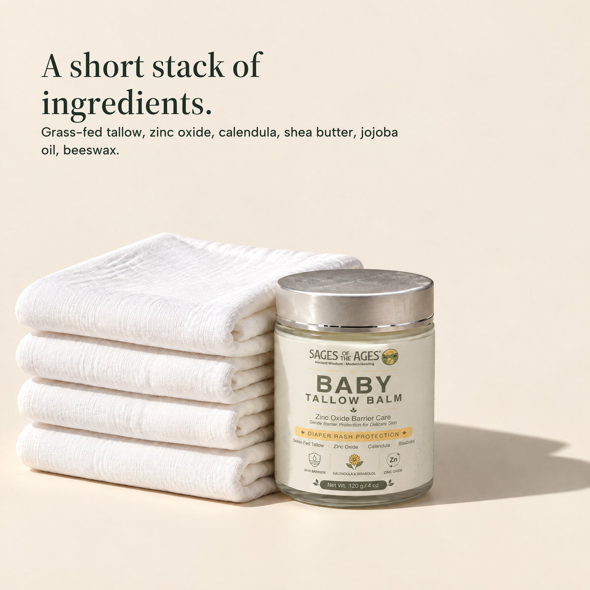 Jar of baby tallow balm beside a stack of folded white cloths. A short stack of ingredients. Grass-fed tallow, zinc oxide, calendula, shea butter, jojoba oil, beeswax.