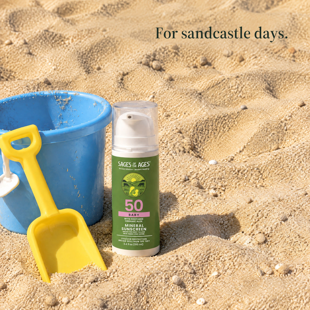 Baby mineral sunscreen pump bottle in the sand beside a blue bucket and yellow spade. For sandcastle days.