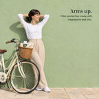 A woman stretches with her hands behind her head beside a bicycle, the deodorant in its basket. Arms up. Odor protection made with magnesium and zinc.