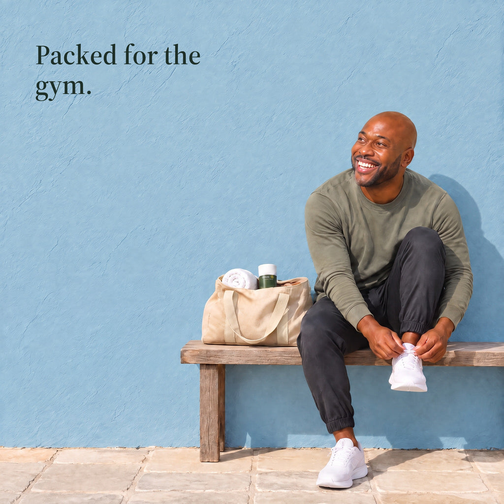 A man ties his shoe on a bench beside a canvas gym bag with the deodorant in it. Packed for the gym.