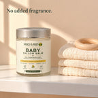 Jar of baby tallow balm on a nursery shelf next to folded muslin cloths and a wooden teething ring. No added fragrance.
