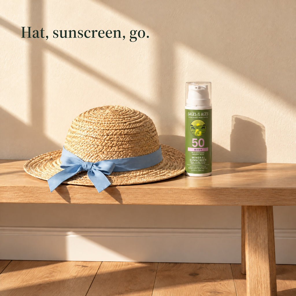 Baby mineral sunscreen pump bottle on a wooden bench next to a straw hat with a blue ribbon. Hat, sunscreen, go.