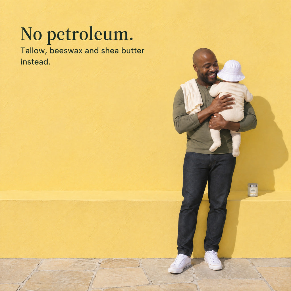 A father holds his baby at his shoulder by a yellow wall, the jar of balm on the ledge beside them. No petroleum. Tallow, beeswax and shea butter instead.