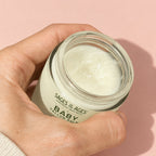 A hand holding the open jar of baby tallow balm.
