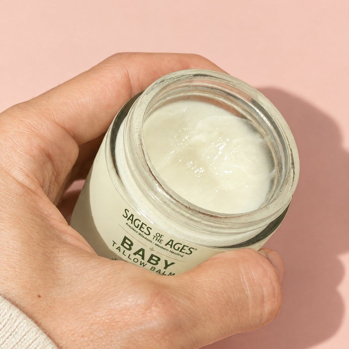 A hand holding the open jar of baby tallow balm.
