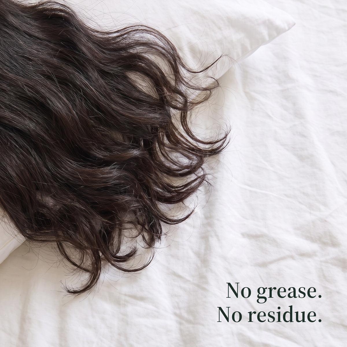 Dark wavy hair spread across white bed linen. No grease. No residue.