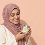 A woman in a pink headscarf smiles down at the jar of baby tallow balm in her hands.
