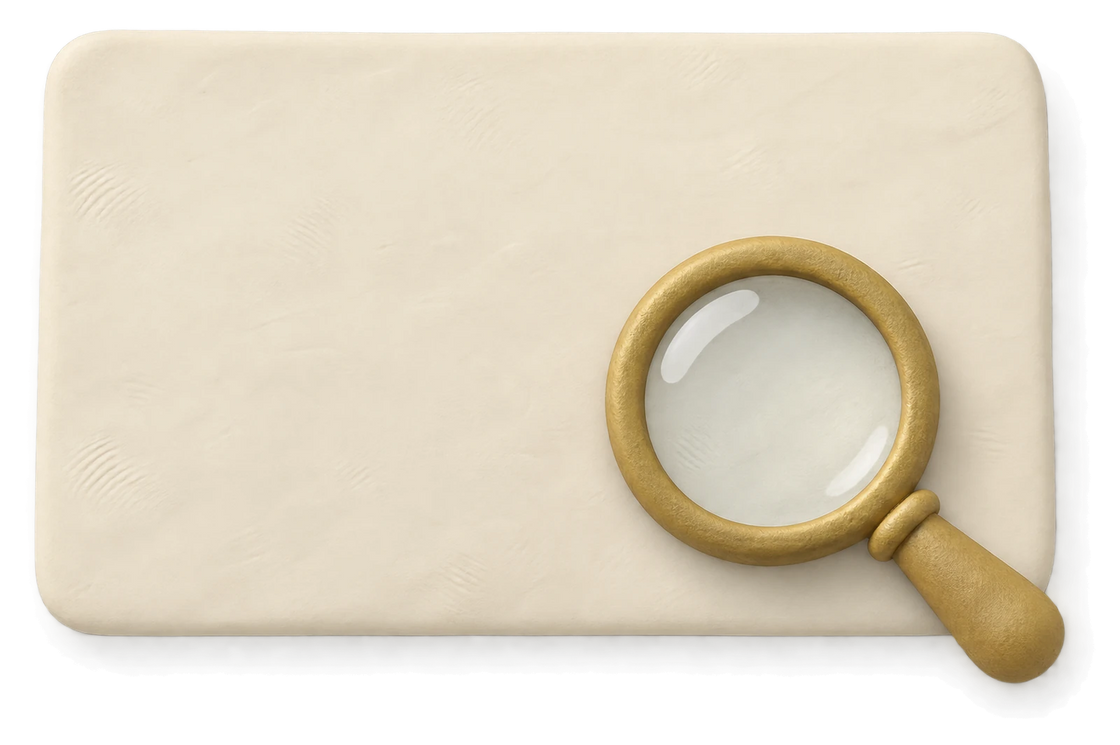 A brass magnifying glass resting on a blank cream clay card